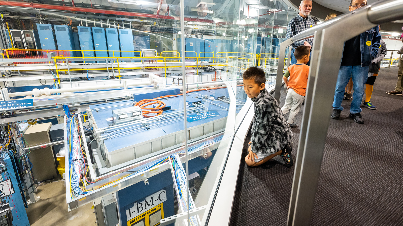 A boy sits on the floor to see instruments below that make up the Advanced Photon Source during a facility tourat Argonne National Laboratory's Open House.