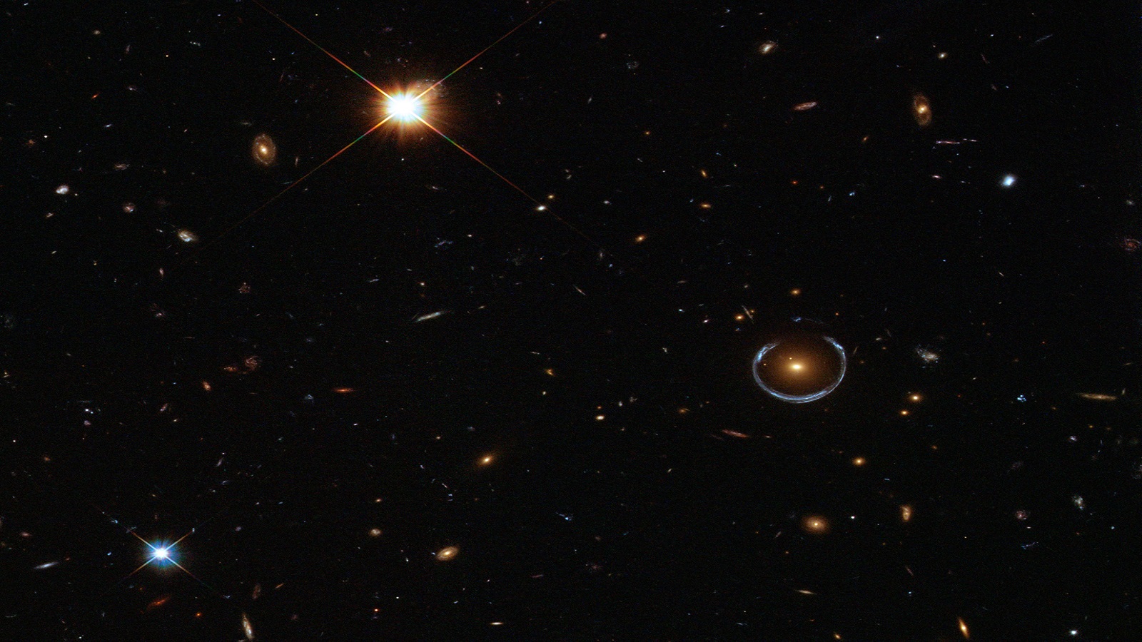 The image shows an Einstein ring (middle right) formed by gravitational lensing of a star-forming galaxy (blue) by a massive luminous red galaxy (orange). This system was first discovered by the Sloan Digital Sky Survey in 2007; the images are from the Hubble Space Telescope. (Image by NASA.) 