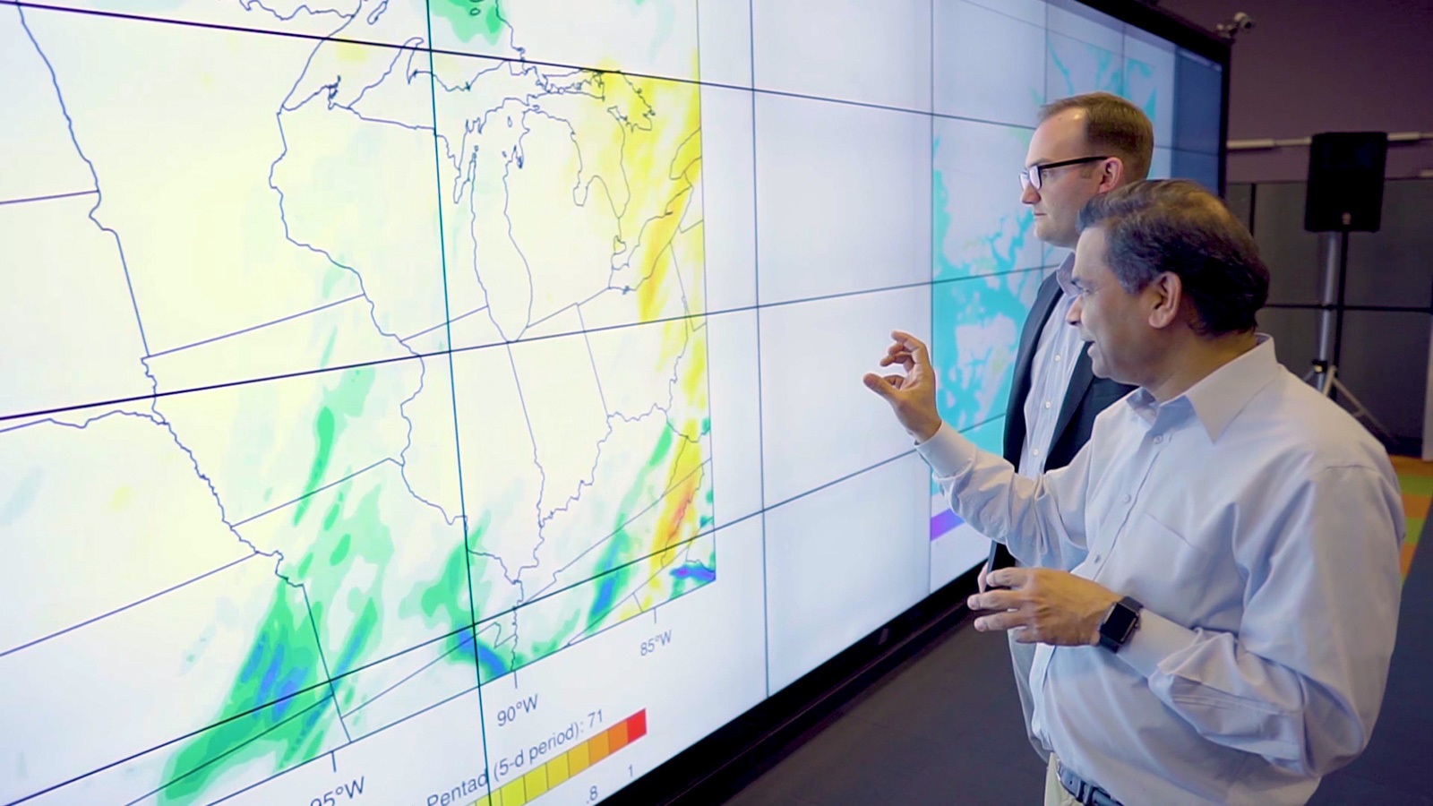 Two men standing in front of a screen with climate map. (Image by Argonne National Laboratory.)