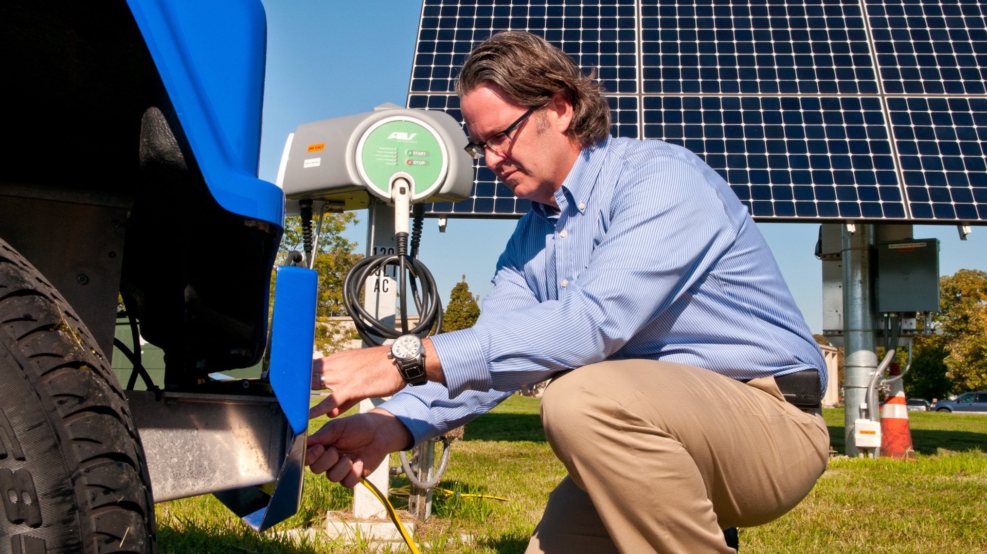 Male scientist kneeling near a vehicle with solar panels in background