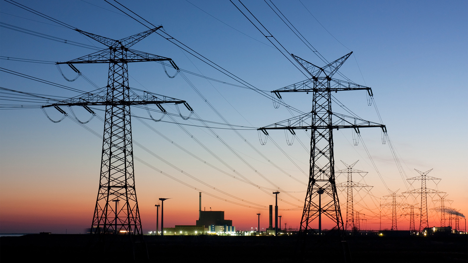 photo of high-voltage powerlines at sunset with wind turbines and nuclear generation plant in background