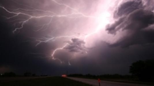Photo of clouds in a darkened sky with a lightning bolt crossing the sky.
