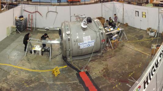 Panorama view of the 4 Tesla solenoid facility with Midhat Farooq and Joe Grange aligning an NMR calibration setup (left of the magnet), Ran Hong and students improving the calibration motion control system (right of the magnet) and David Flay analyzing current NMR calibration data. (Image by Argonne National Laboratory.)