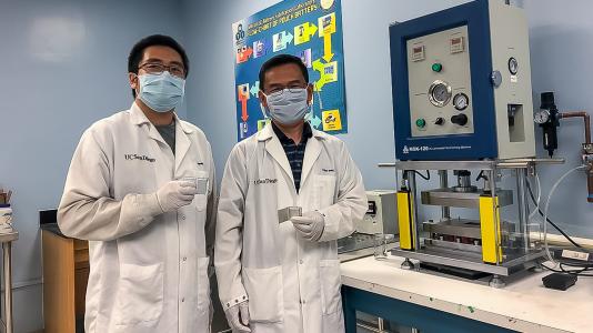 UC San Diego researchers Haodong Liu and Ping Liu hold batteries made with the disordered rocksalt anode material they discovered, standing in front of a device used to fabricate battery pouch cells. (Image by University of California San Diego.)