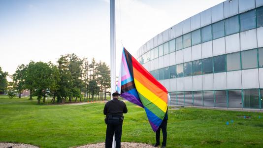 Photo of two men raising rainbow-colored flag on flag pole. (Image by Argonne National Laboratory.)
