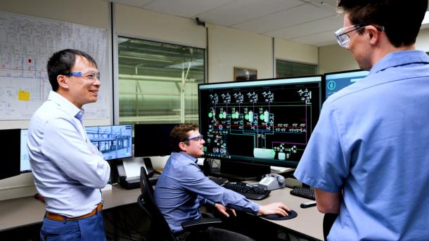 Scientist Bo Feng stands near computer screens and discusses fast reactor technology in experimental facility control room.
